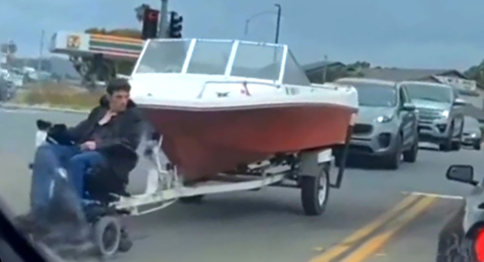 A man in a wheelchair pulls a motorboat down a California road